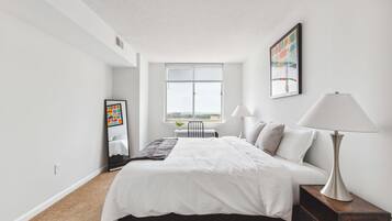 Un dormitorio moderno con una cama grande, una mesita de noche con lámpara, una ventana con persianas y un cuadro enmarcado en la pared.