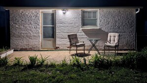 Una pequeña casa de ladrillo con un patio, dos sillas y una mesa.
