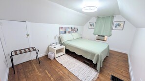Une petite chambre bien rangée, avec un lit simple, une table de chevet, une chaise, un radiateur et une fenêtre avec des rideaux.