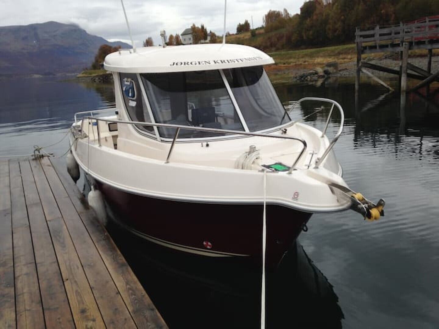 A boat docked at a wooden pier with a mountainous backdrop.