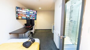 A hotel room with a bed, a desk with a laptop, a flat-screen TV displaying various channels, and a shower area. - Charming 1-bed Studio in Birmingham (Birmingham)