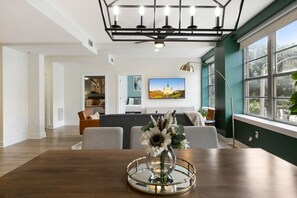 A modern living room with a wooden dining table, a sofa set, and a large window with a view of greenery. - Timeless Elegance: 4BR Luxury Condo in New Orleans (New Orleans)