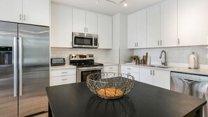 Una cocina moderna con armarios blancos, electrodomésticos de acero inoxidable y una encimera negra con una cesta de alambre.