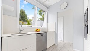 A modern kitchen with a built-in dishwasher, a window with a view of greenery, and a white door. - Peaceful & Light Paddington home (Paddington)