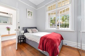 Une chambre à coucher comprenant un lit, une table de chevet, une commode, une fenêtre et une porte donnant sur une autre pièce.