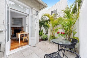 An open door leading to a room with a fireplace, a dining table, and chairs. Outside, there is a patio with a table, chairs, and potted plants. - Peaceful & Light Paddington home (Paddington)