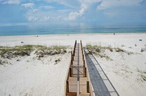 Une promenade en bois menant à une plage, avec un ciel dégagé et une mer calme.