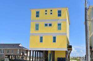 Un edificio amarillo de dos pisos con base blanca, múltiples ventanas y un balcón.