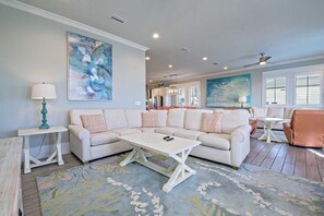 A living room with a white sectional sofa, a coffee table, and a rug. There are two paintings on the walls and a ceiling fan. - Lemonshello BeachFront, Hot tub, Heated Pool, 8 bedrooms (Gulf Shores)