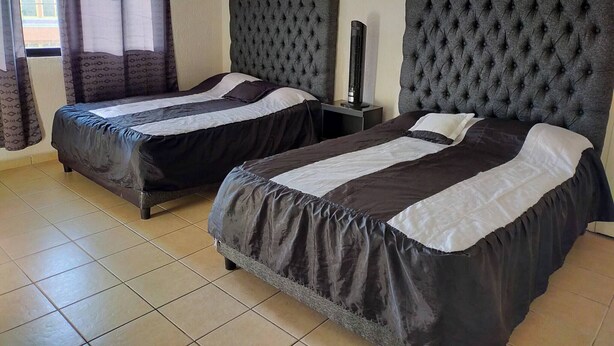 A hotel room with two beds, a standing heater, and a window with curtains. - Cozy Villa in Almoloya de Juárez, Mexico (Almoloya de Juárez)