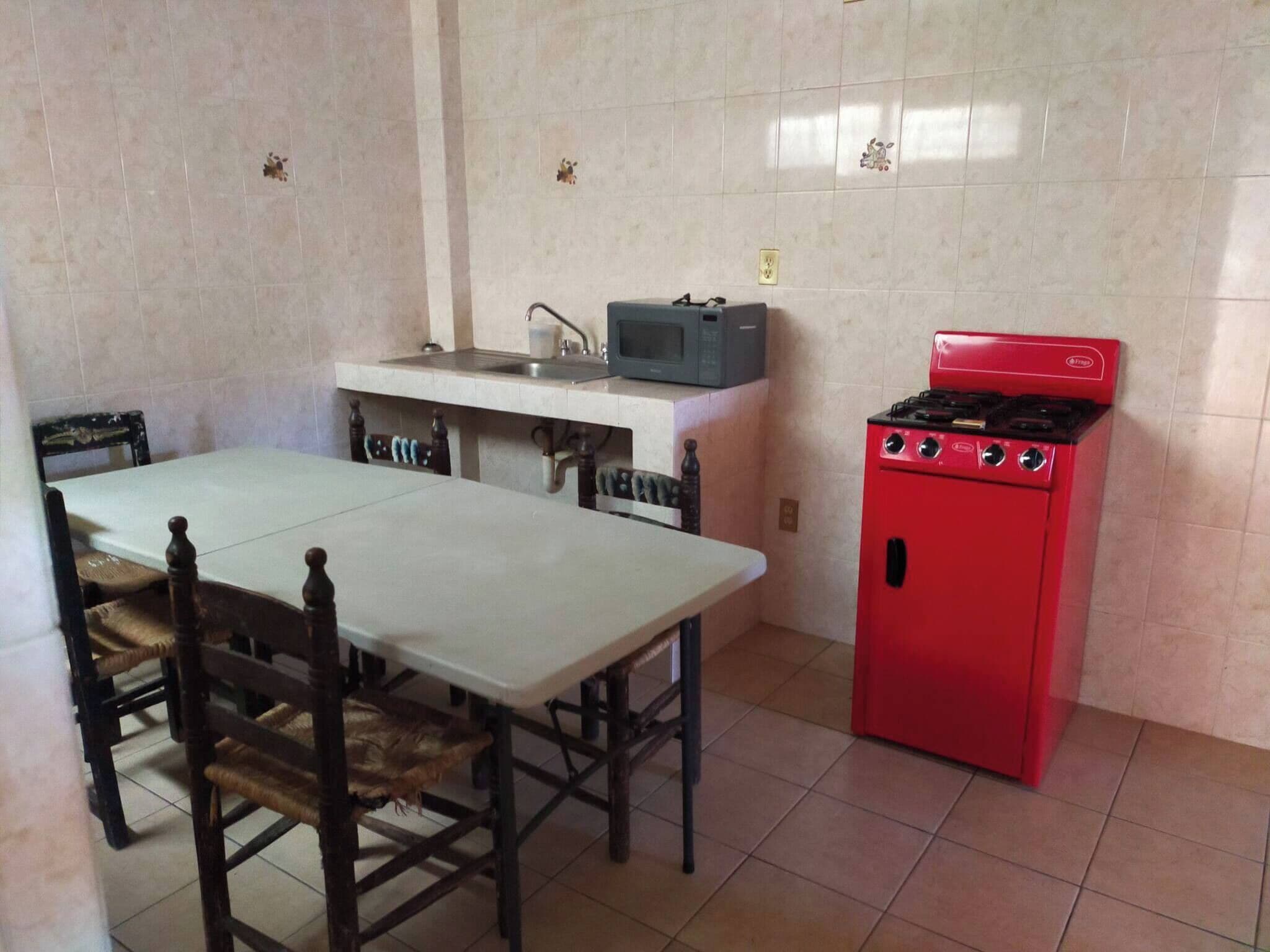 Cocina compacta con mesa, sillas, pileta, microondas y estufa roja.