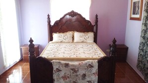 A bedroom with a wooden bed, floral bedspread, and a view of the outside through a window. - The Beauty of Samana (Samaná)