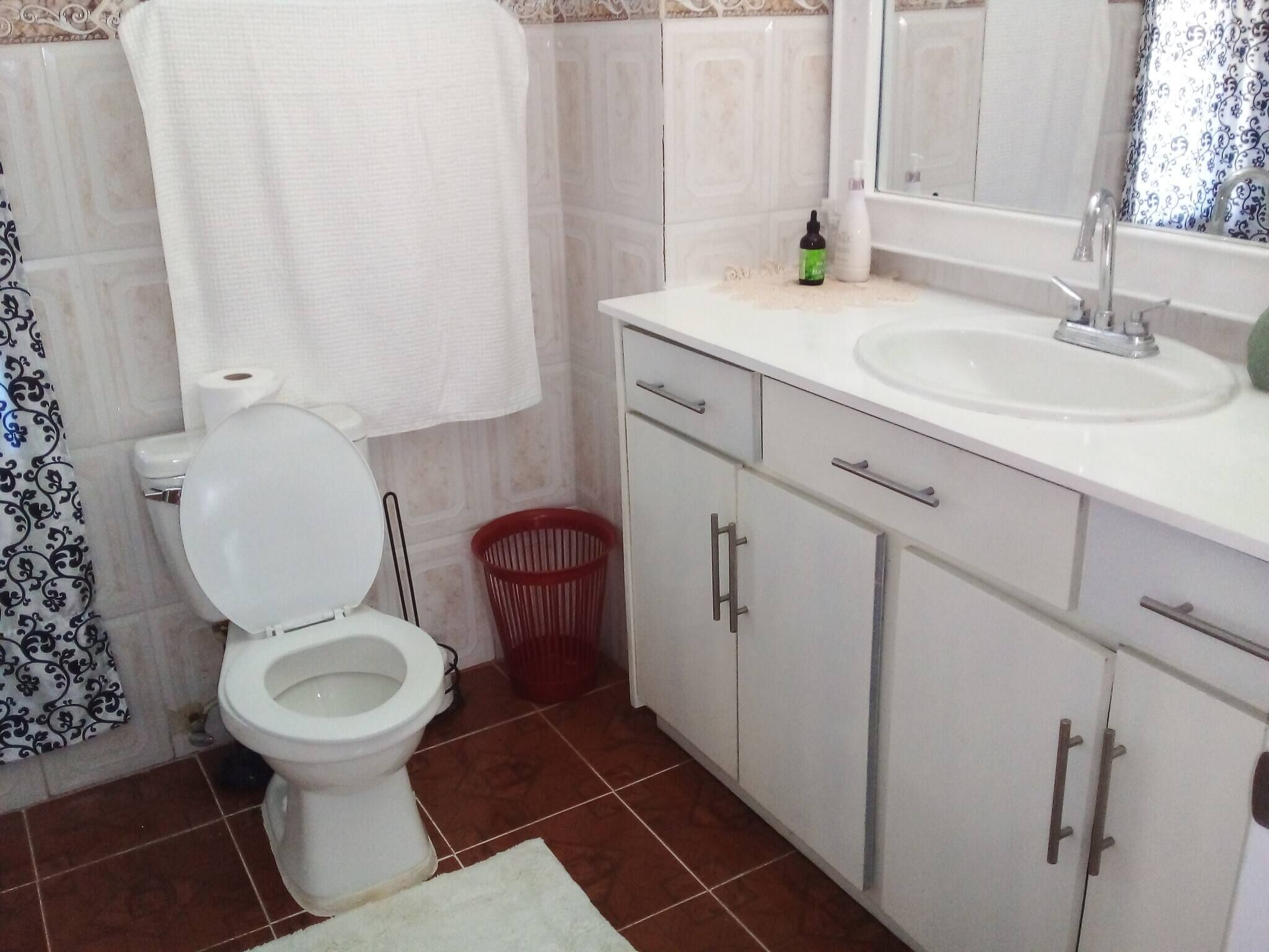 A bathroom with a toilet, sink, mirror, and cabinets.