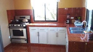 A kitchen with a stove, oven, white cabinets, a sink, and a window. - The Beauty of Samana (Samaná)