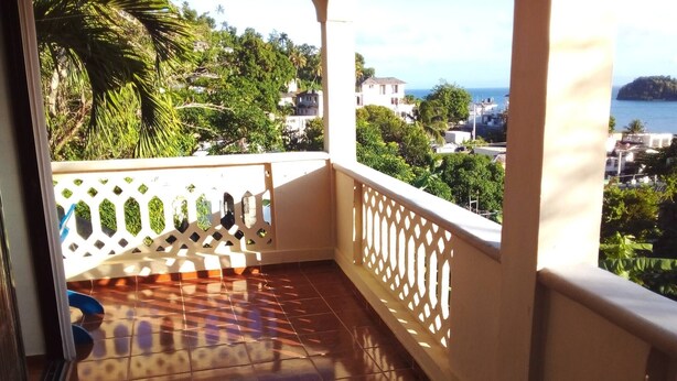 A balcony with a tiled floor, white railing, and a view of a coastal town. - The Beauty of Samana (Samaná)