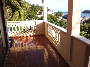 Un balcon doté d’un sol carrelé, d’une balustrade blanche et offrant une vue sur une ville côtière.