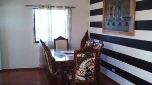 A dining area with a wooden table and chairs, a window with curtains, and a striped wall with a framed picture. - The Beauty of Samana (Samaná)