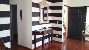 A hallway with a black and white striped wall, a wooden bench, a mirror, and a door. - The Beauty of Samana (Samaná)