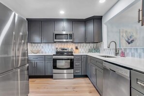 A modern kitchen with stainless steel appliances, grey cabinets, and a white countertop.