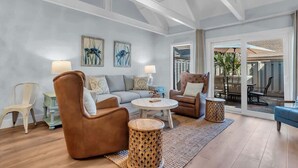 Een ruime woonkamer met een hoge plafond, een zithoek, een salontafel, en uitzicht door een glazen deur op een terras.