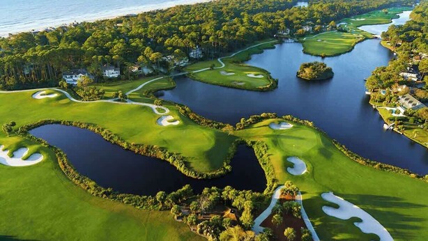 Een golfbaan met waterhindernissen, zandbakken en uitzicht op de oceaan.