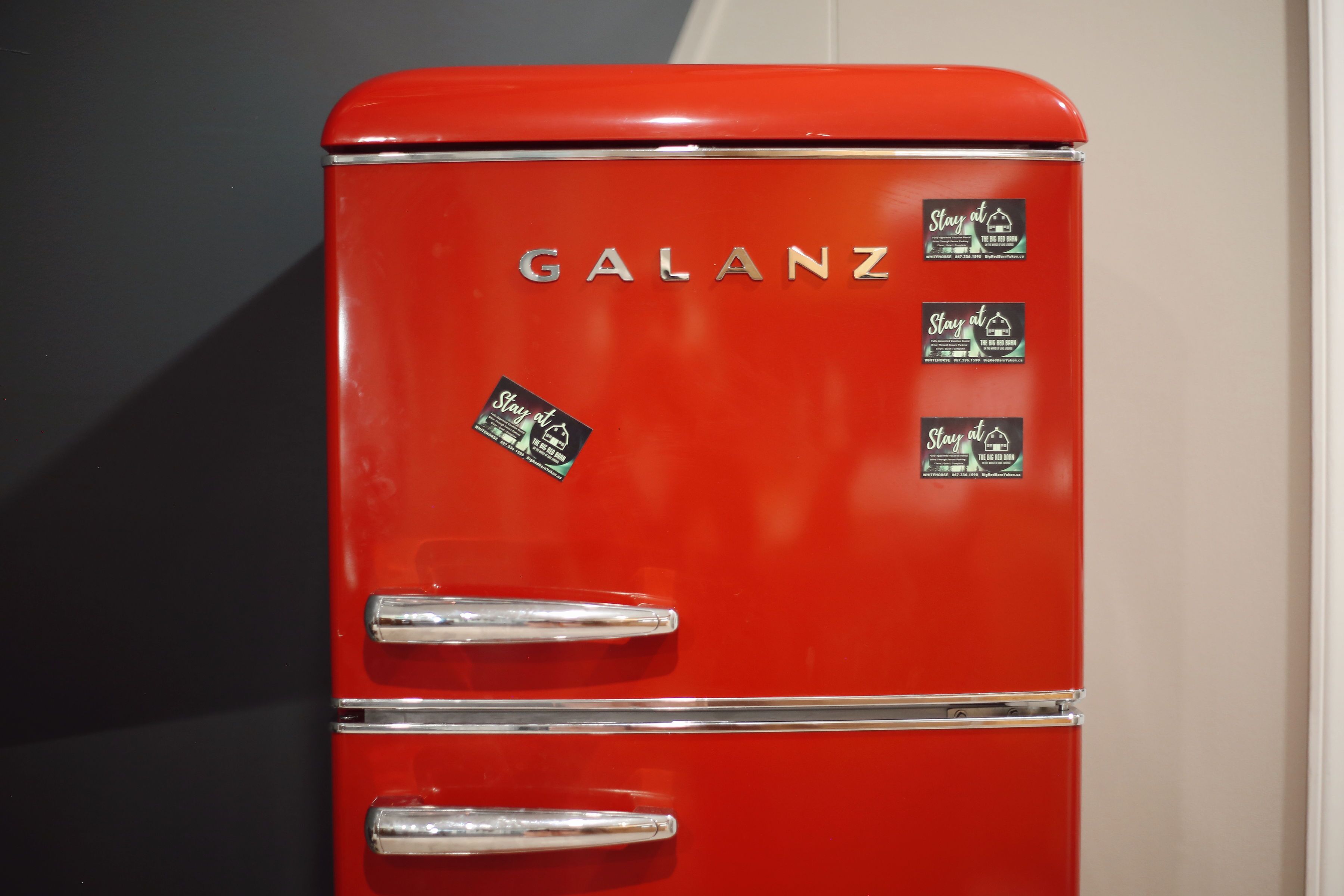 Un refrigerador Galanz rojo con dos puertas y tres pegatinas en la parte frontal.