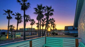 A balcony with a view of palm trees and a sunset. - Big Yard w/ Priv Pool, Firepit, Patio Near the Beach Reel Time by Avantstay (Port Aransas)