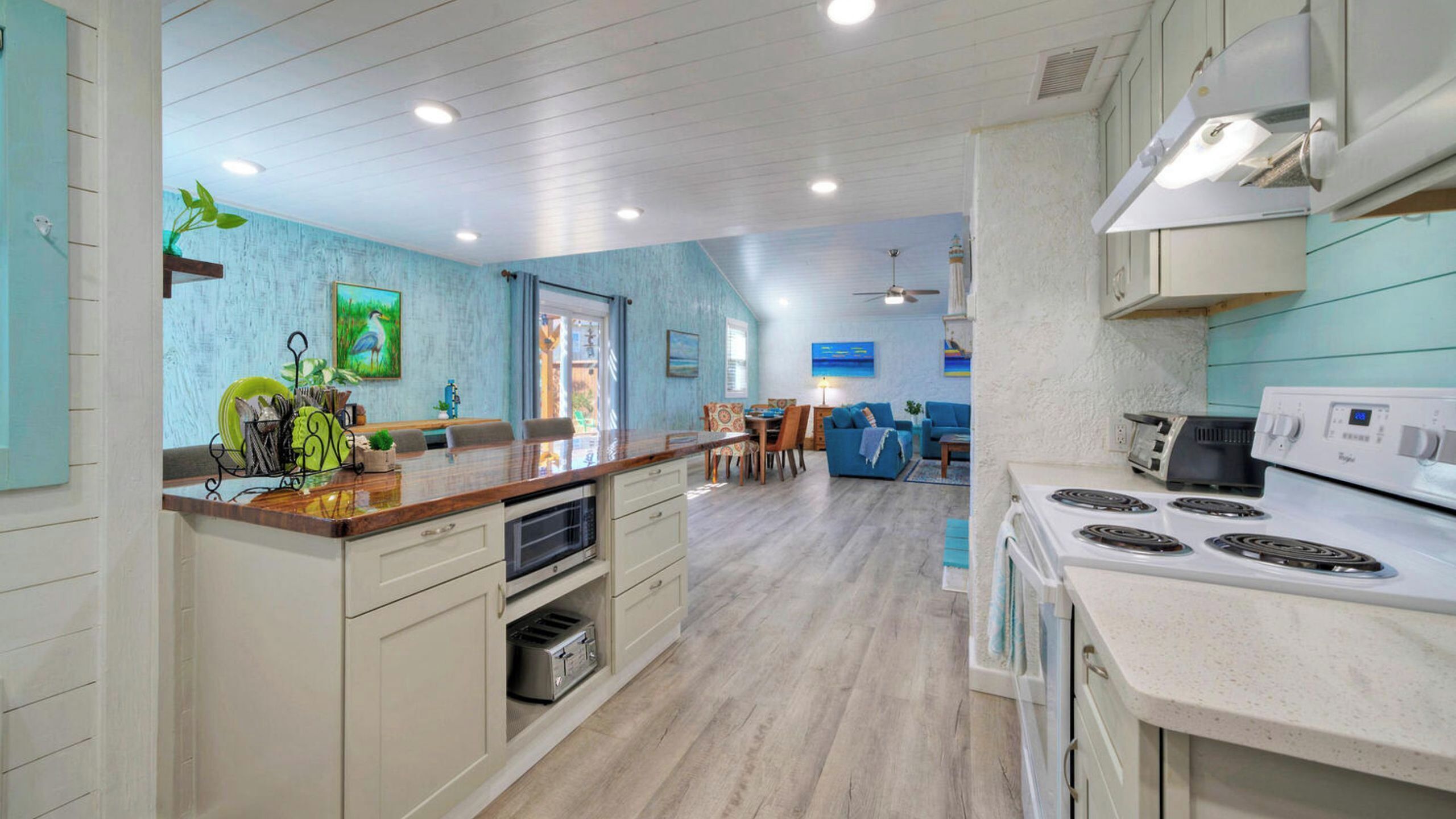 Een moderne keuken met een centraal eiland, een eethoek met een blauwe bank en een woonkamer met een televisie.