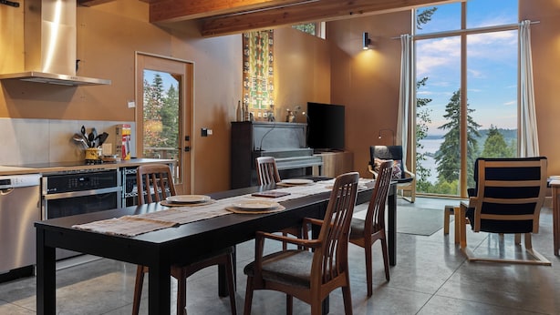A modern kitchen with a dining area, large windows, and a view of the outdoors. - Crows Nest by Avantstay Accessible Home w/ Views (Clinton)
