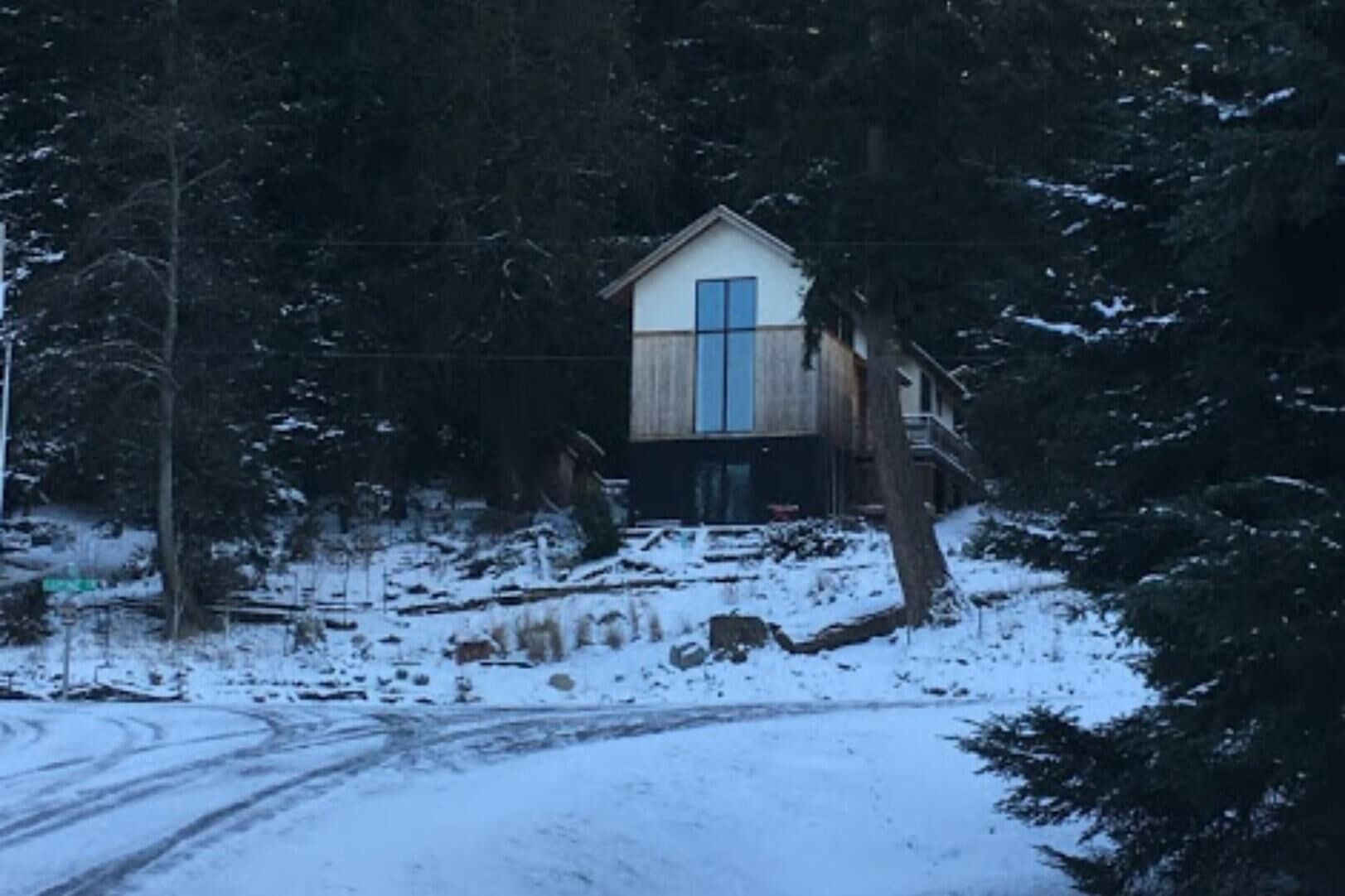 A two-story cabin with a large window on the upper floor, surrounded by snow-covered ground and trees.