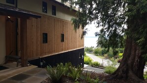 A modern building with a wooden facade, a visible entrance, and a view of a road leading to a body of water. - Crows Nest by Avantstay Accessible Home w/ Views (Clinton)