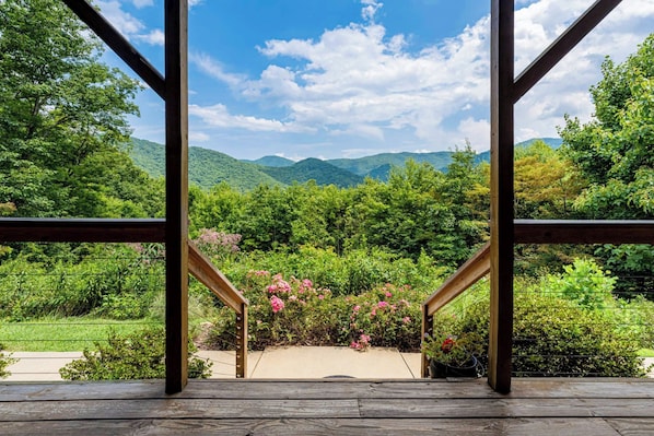 Una escalera de madera que lleva a un balcón con vistas a un jardín exuberante y montañas distantes.