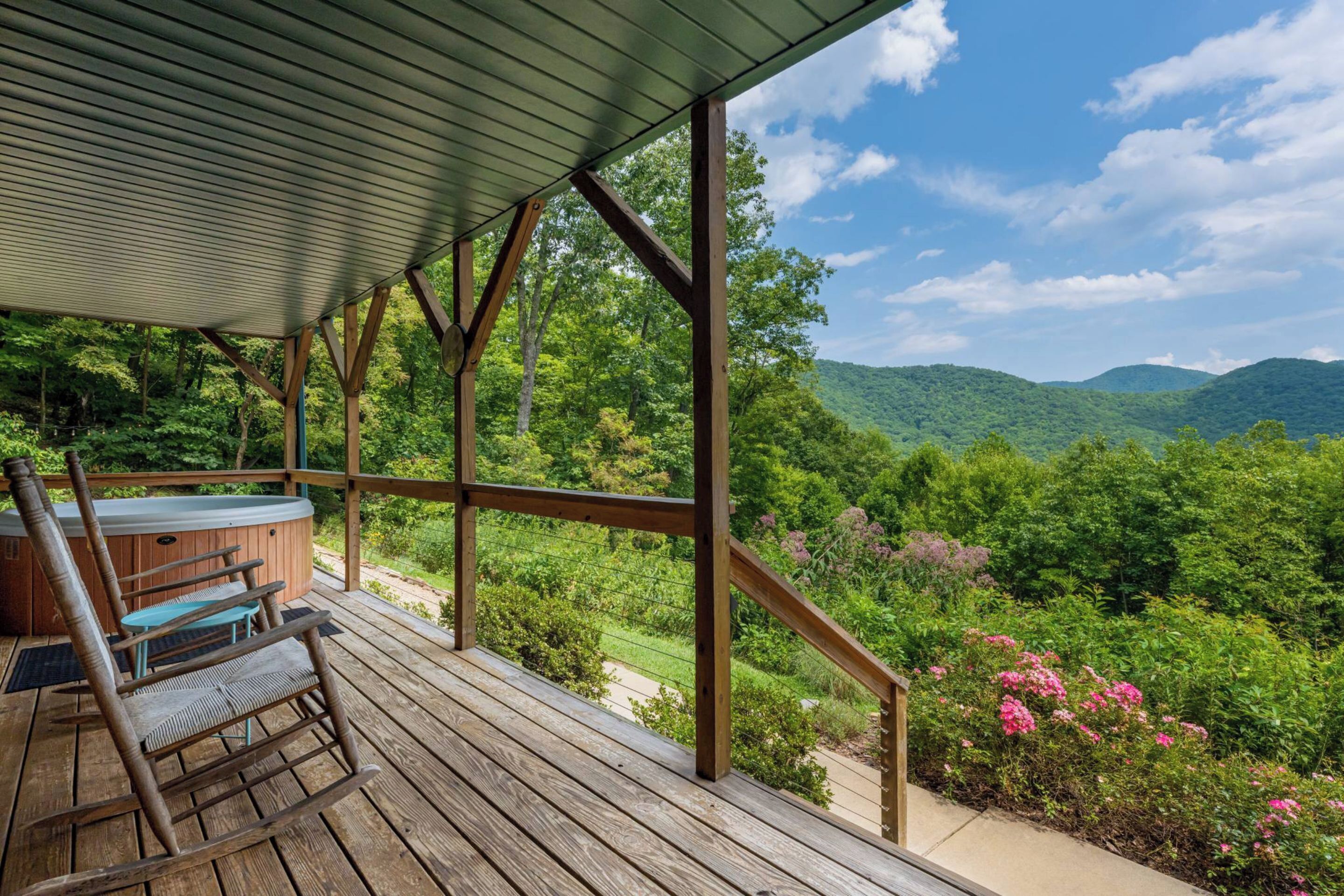 Une terrasse en bois avec un jacuzzi, une chaise berçante et une table.