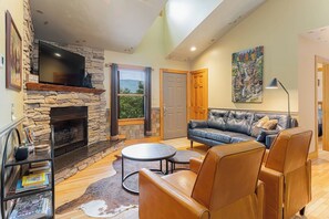 Una sala de estar con chimenea de piedra, sofá de cuero y televisor de pantalla plana montado en la pared.
