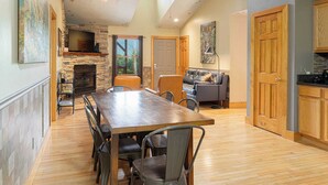 A spacious living area with a stone fireplace, a dining table with chairs, a sofa, and a television mounted on the wall. - Among the Clouds by Avantstay Views + Hot Tub (Candler)