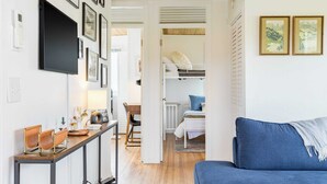 A modern living room with a blue sofa, a wooden dining table with chairs, and a kitchen area with a white countertop and appliances. - Swan Lake Cottage by Avantstay Views + Firepit (Oak Harbor)