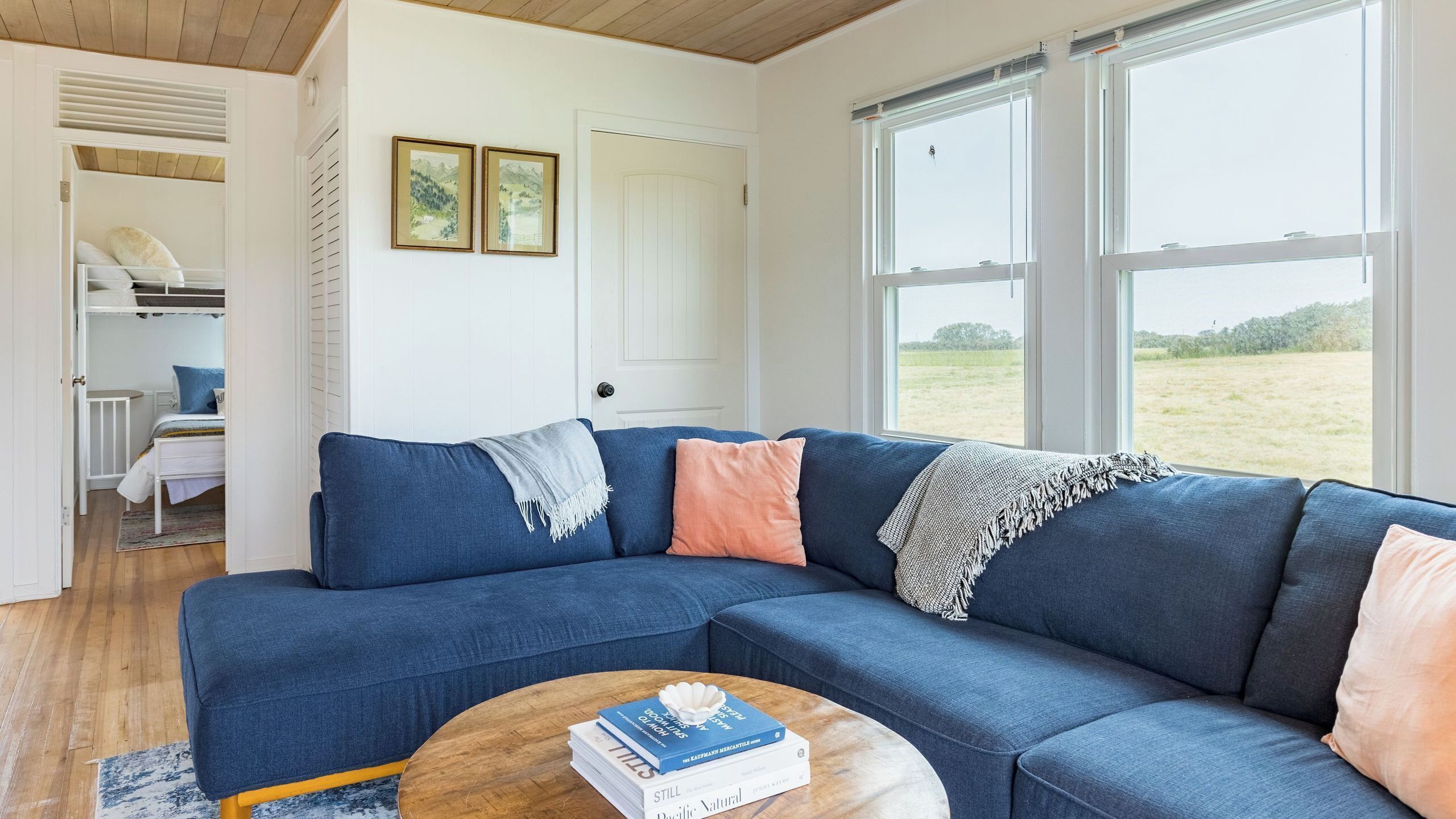A living room with a blue sectional sofa, a wooden coffee table, and a view of a field through large windows.