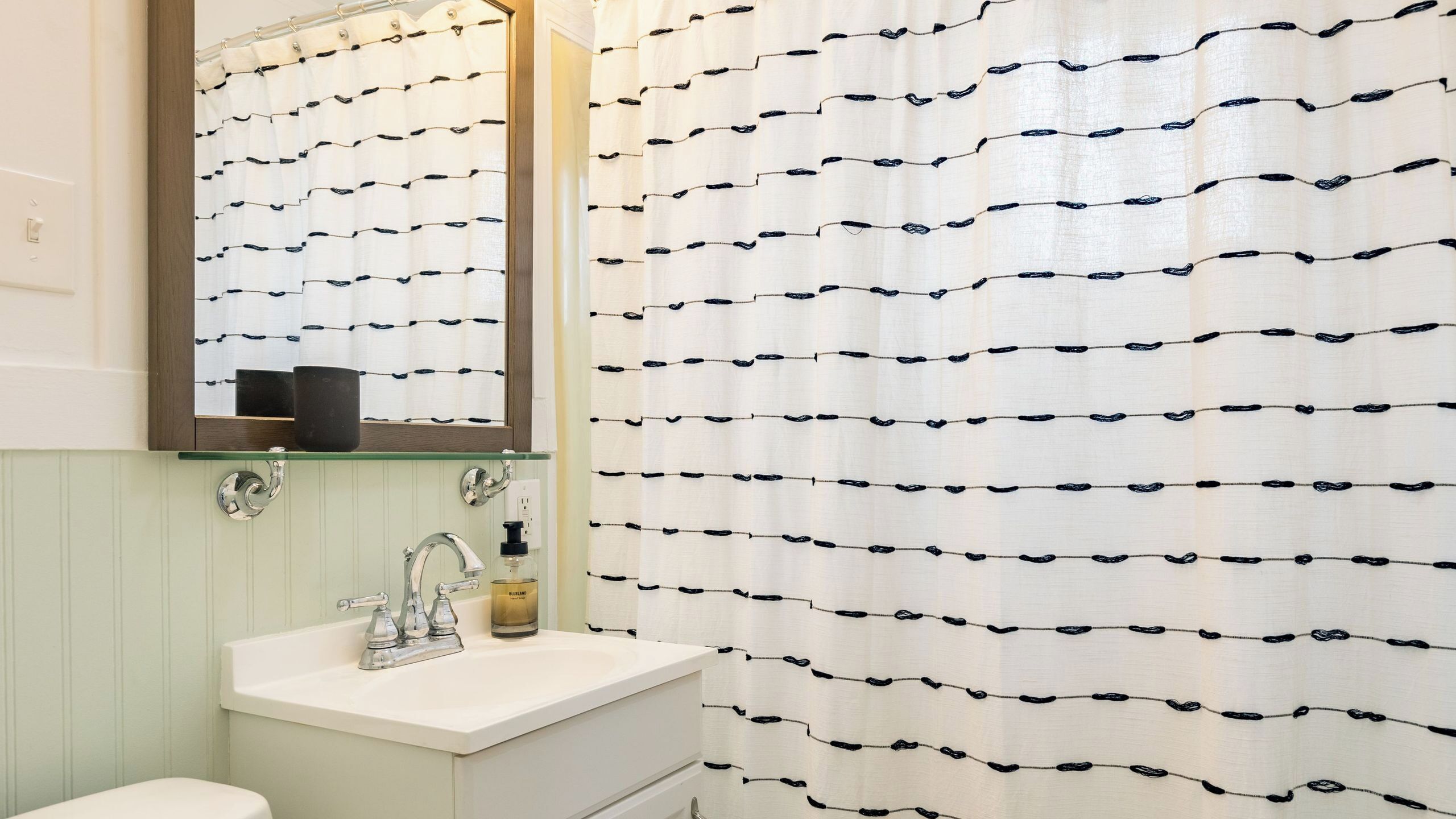 Une salle de bain avec un lavabo blanc, un miroir au-dessus et un rideau de douche à motifs noirs.