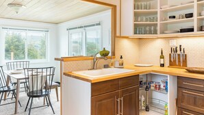 A kitchen with a wooden countertop, a sink, and a window. There is a dining table with chairs and a window with a view of trees. - Swan Lake Cottage by Avantstay Views + Firepit (Oak Harbor)