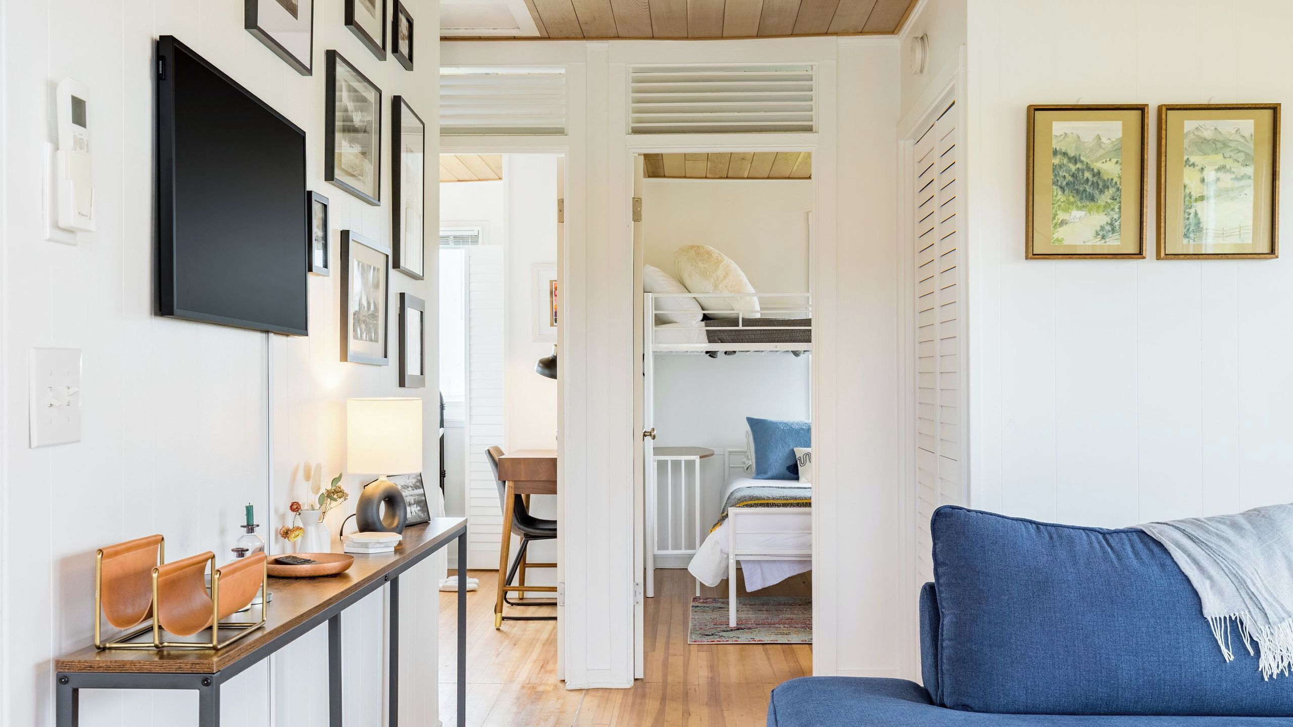 Ein modernes Interieur mit Holzboden, einer Couch, einem Essbereich mit Tisch und Stühlen sowie einem Hochbett im Hintergrund.