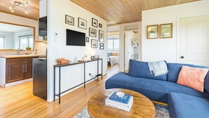 A modern living room with a blue sofa, wooden flooring, and a ceiling fan. - Swan Lake Cottage by Avantstay Views + Firepit (Oak Harbor)