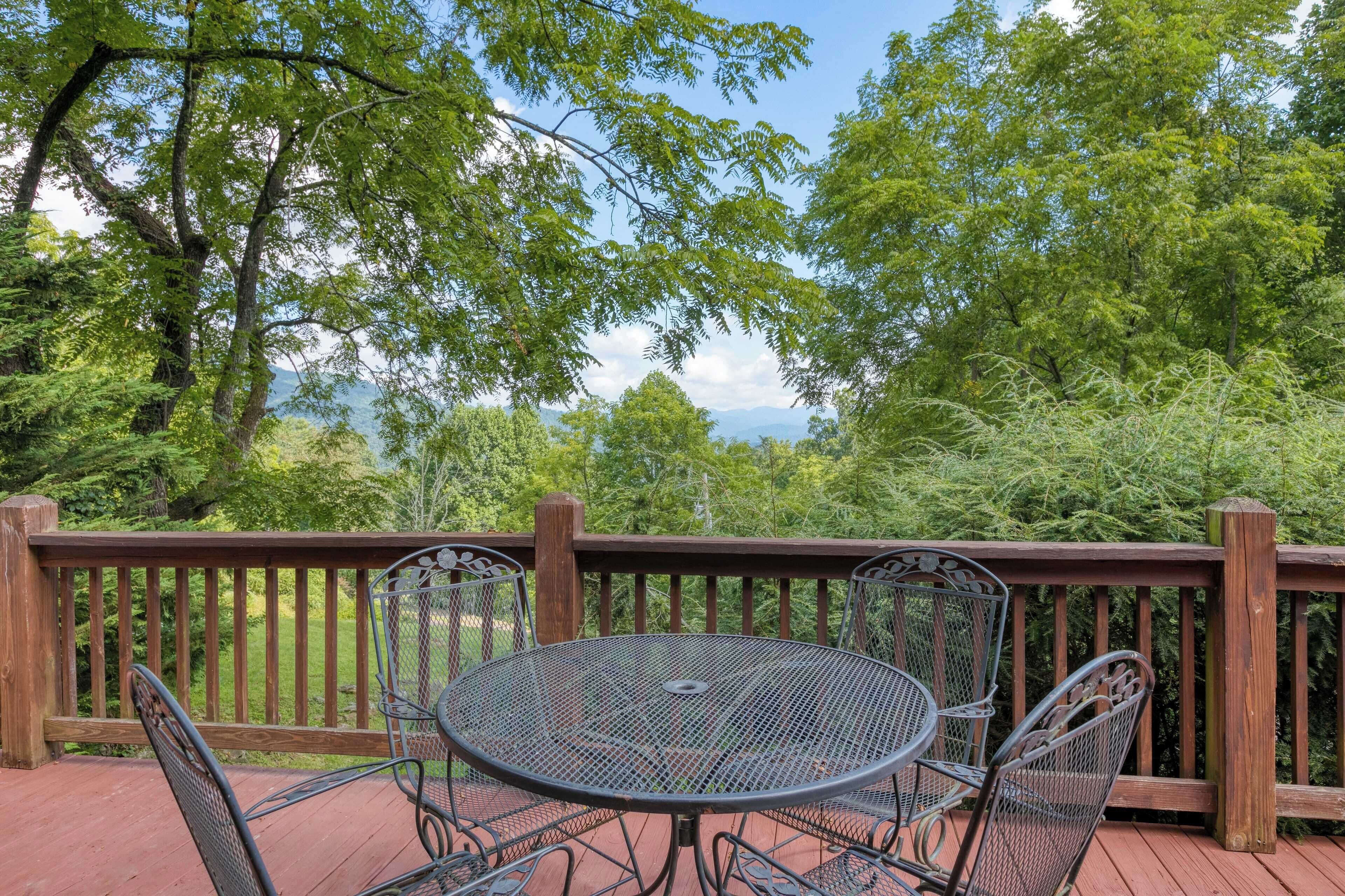 A deck with a metal table and chairs, surrounded by a wooden railing, overlooking a forested area.