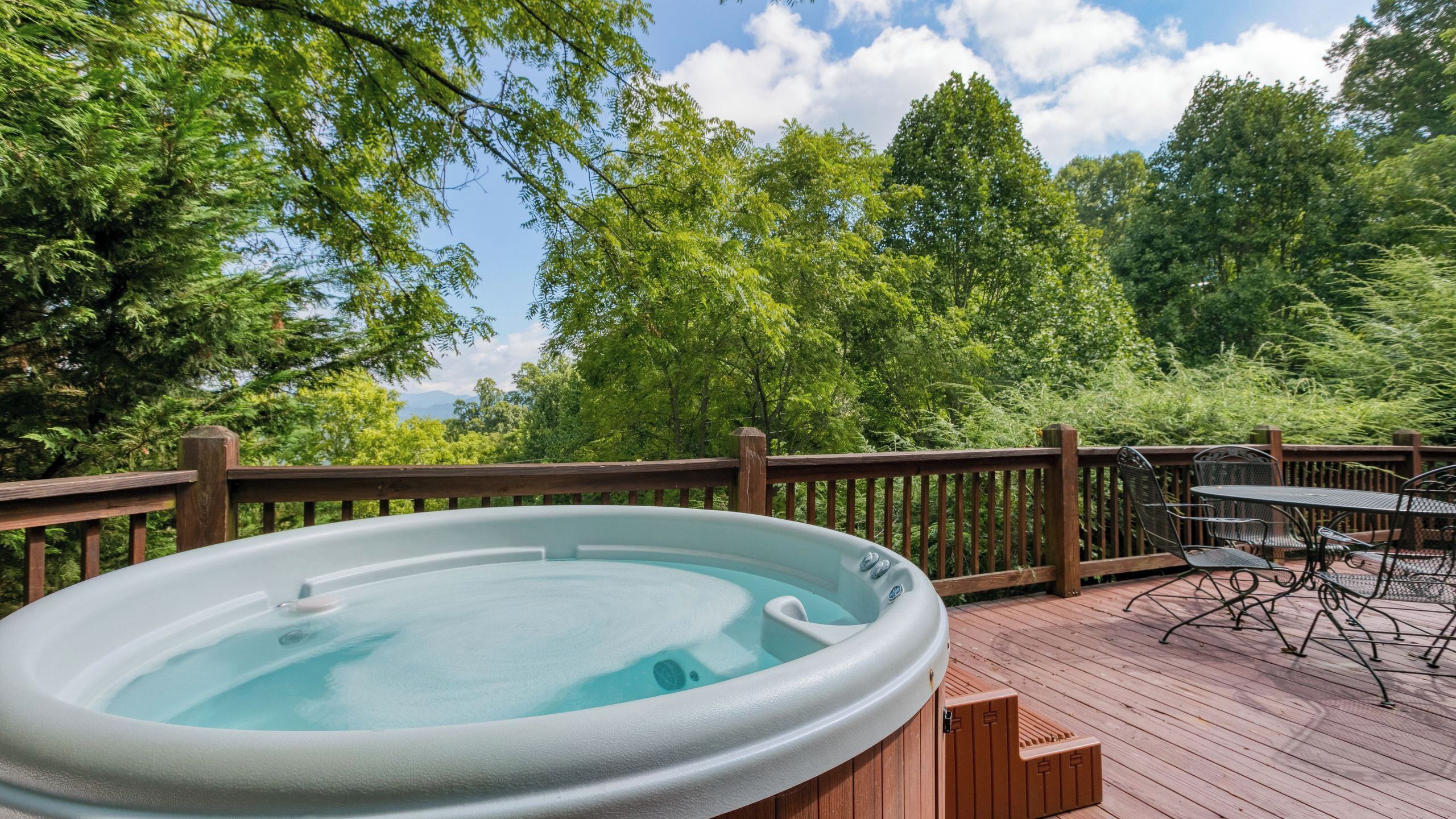 A hot tub on a wooden deck with a view of trees and a clear sky.