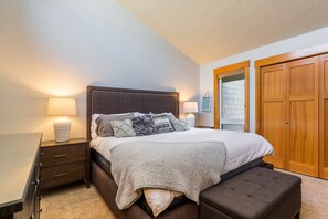 A bedroom with a bed, bedside tables, a nightstand, a wooden wardrobe, and a window with a view.