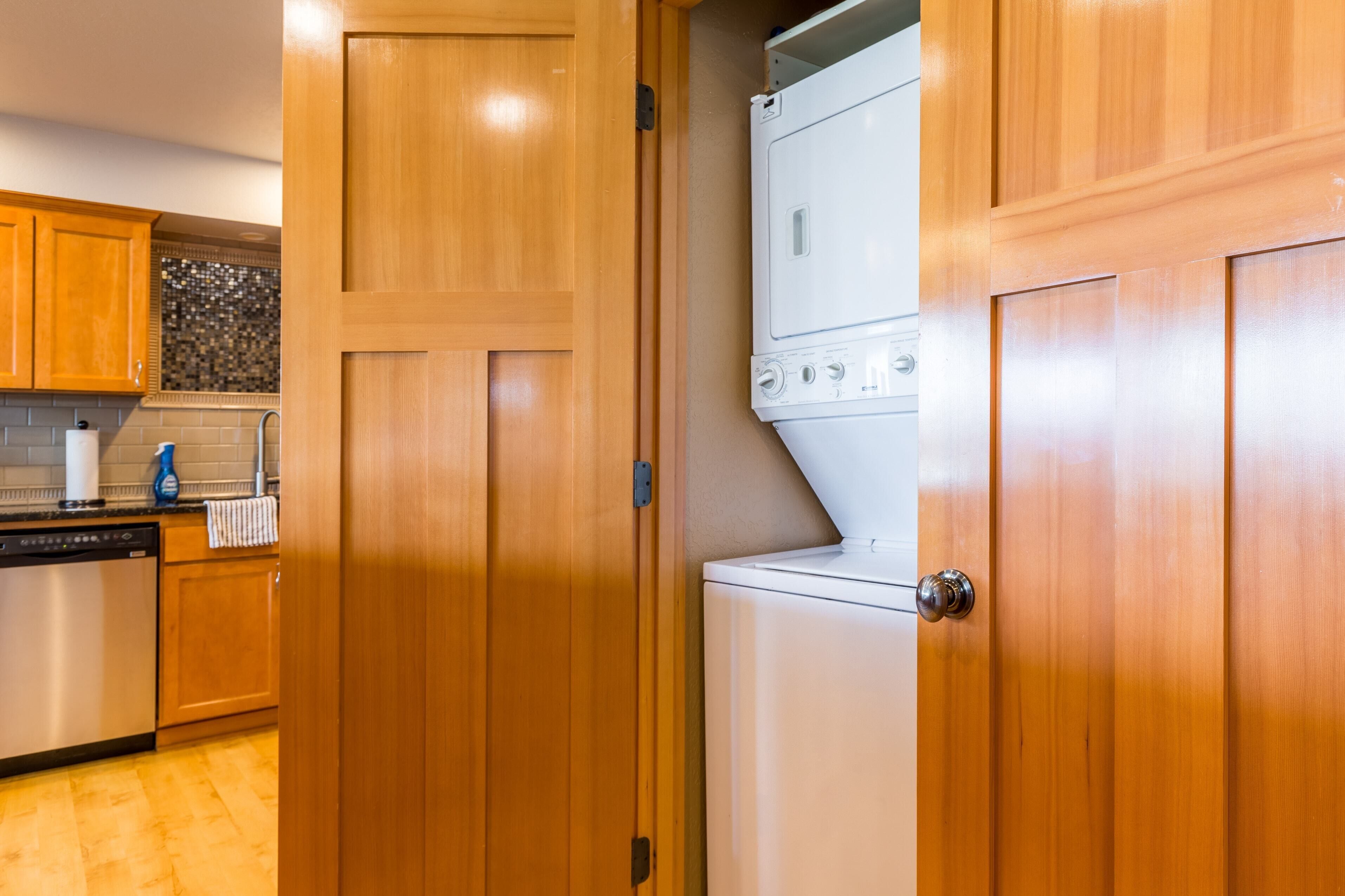 A compact kitchen with wooden cabinets, a dishwasher, and a stacked washer and dryer.
