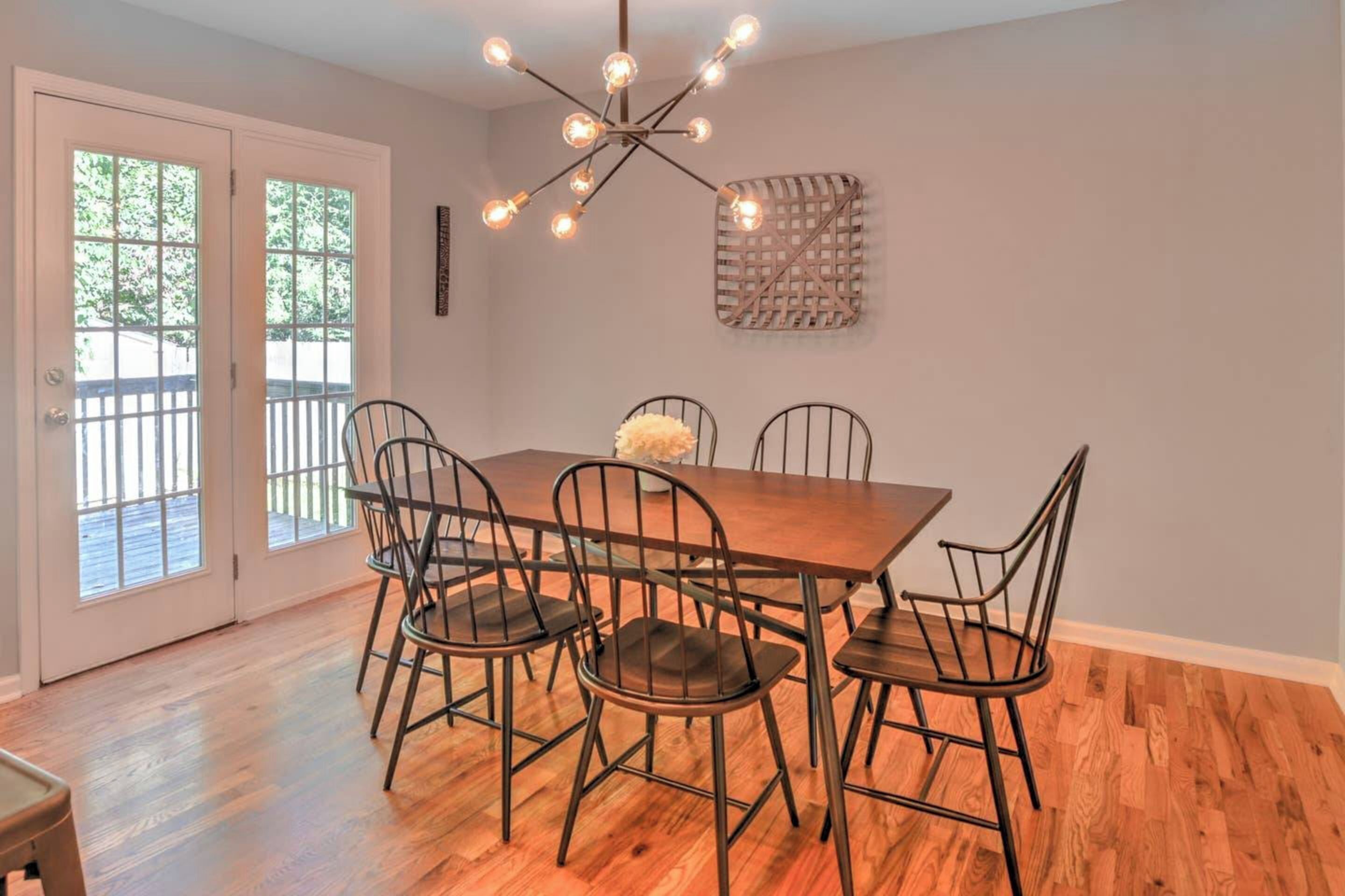 A dining area with a wooden table and metal chairs, a chandelier, and a view through glass doors.