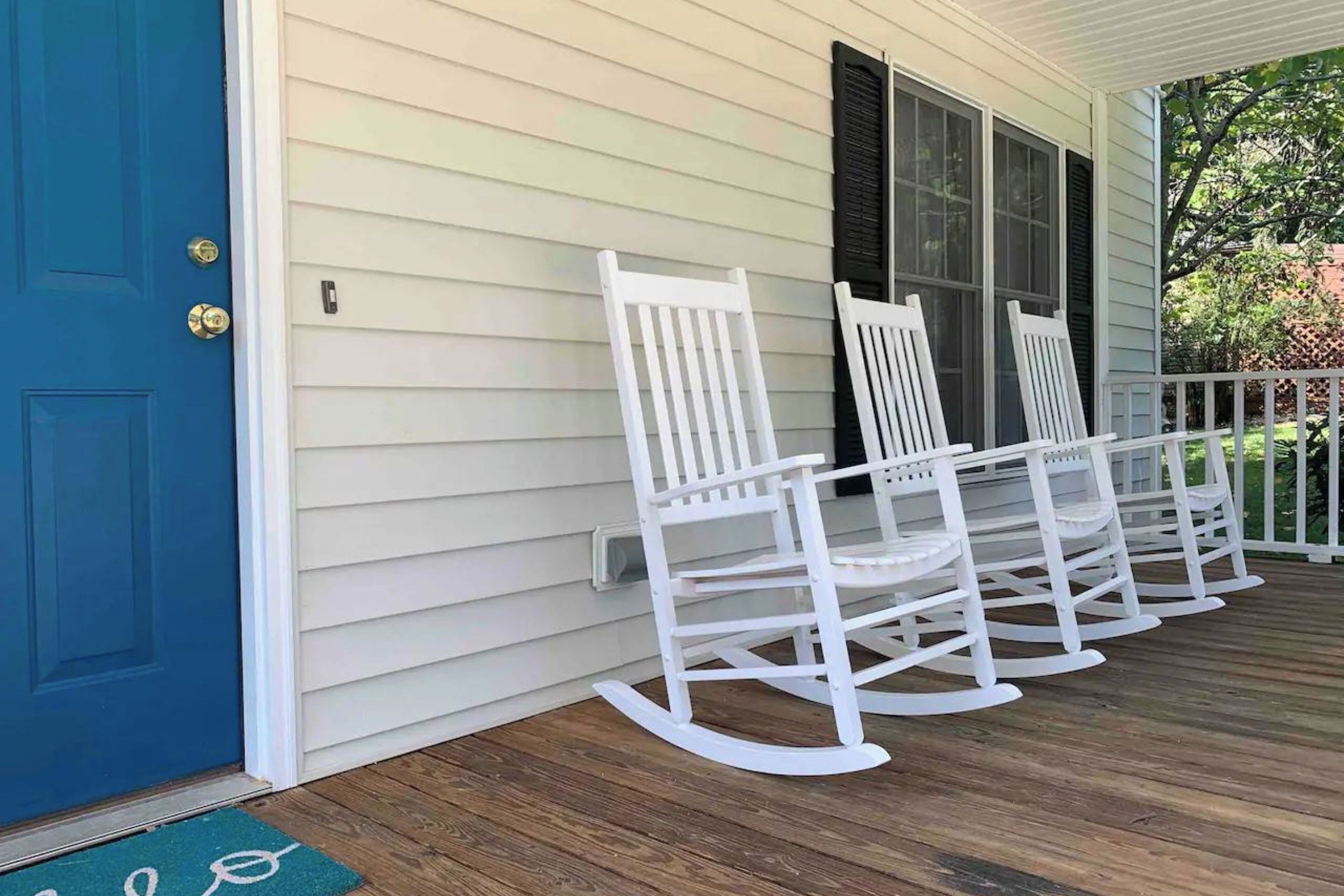 A porch with white rocking chairs and a blue door.