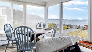En matplats med ett bord och stolar, stora fönster med utsikt över en sjö eller ett annat vattendrag och en brygga, samt utsikt över ett skogsområde.