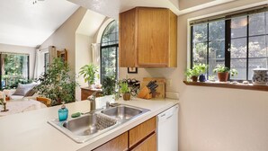 Une cuisine avec des meubles de rangement en bois, un évier et une fenêtre ornée de plantes.