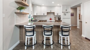 A modern kitchen with white cabinets, a central island with bar stools, and a built-in oven. - Amazing location with private hot tub, sauna, laundry and ground level suite.  (Silver Star Mountain)